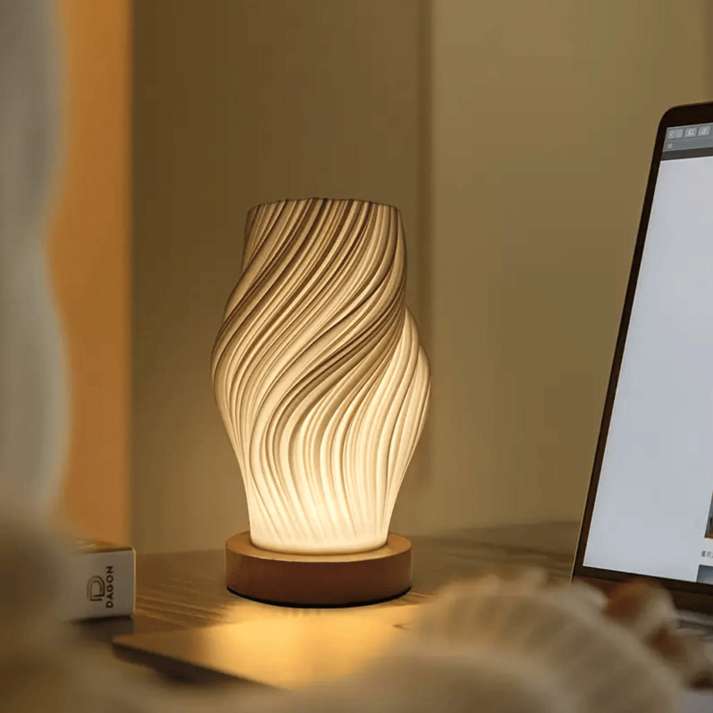 Moderne tafellamp met gedraaid design en warm licht op een bureau naast een laptop.