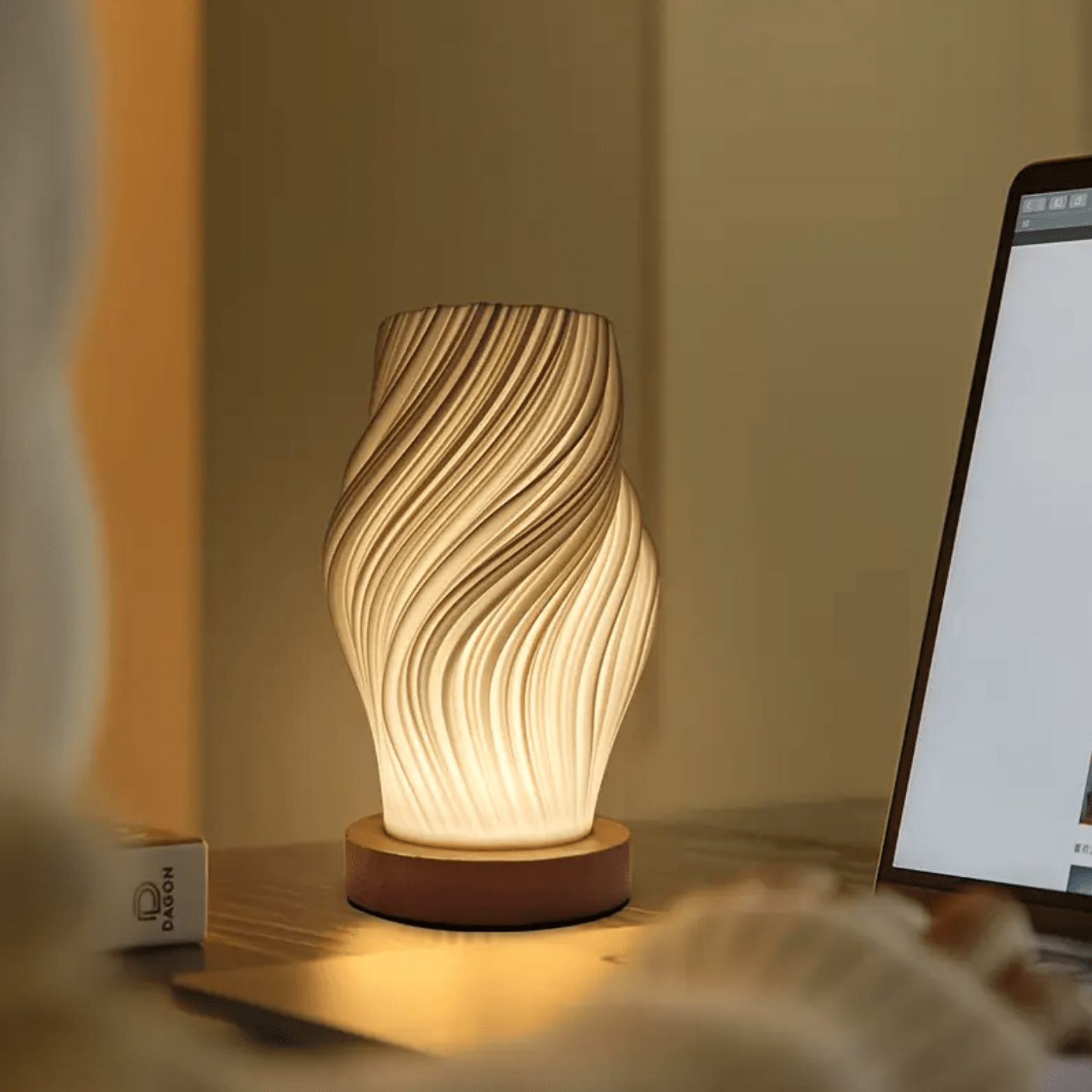 Moderne tafellamp met gedraaid design en warm licht op een bureau naast een laptop.