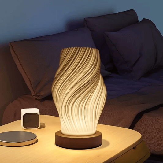 Design tafellamp met gedraaid patroon en warm wit licht op een nachtkastje naast het bed.