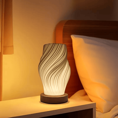 Sfeervolle design tafellamp met golvend patroon en warm licht op een slaapkamerkastje.