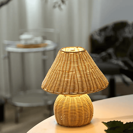 Rotan tafellamp met handgevlochten kap en warme gloed op een lichte tafel in een woonkamer.